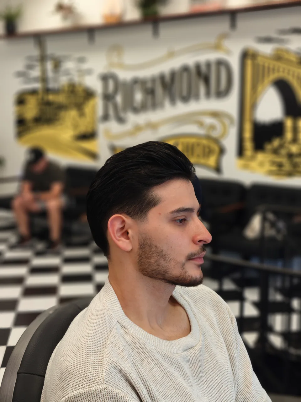 Dark side-parted hair with a smooth swept-back finish and a short beard, shown in profile