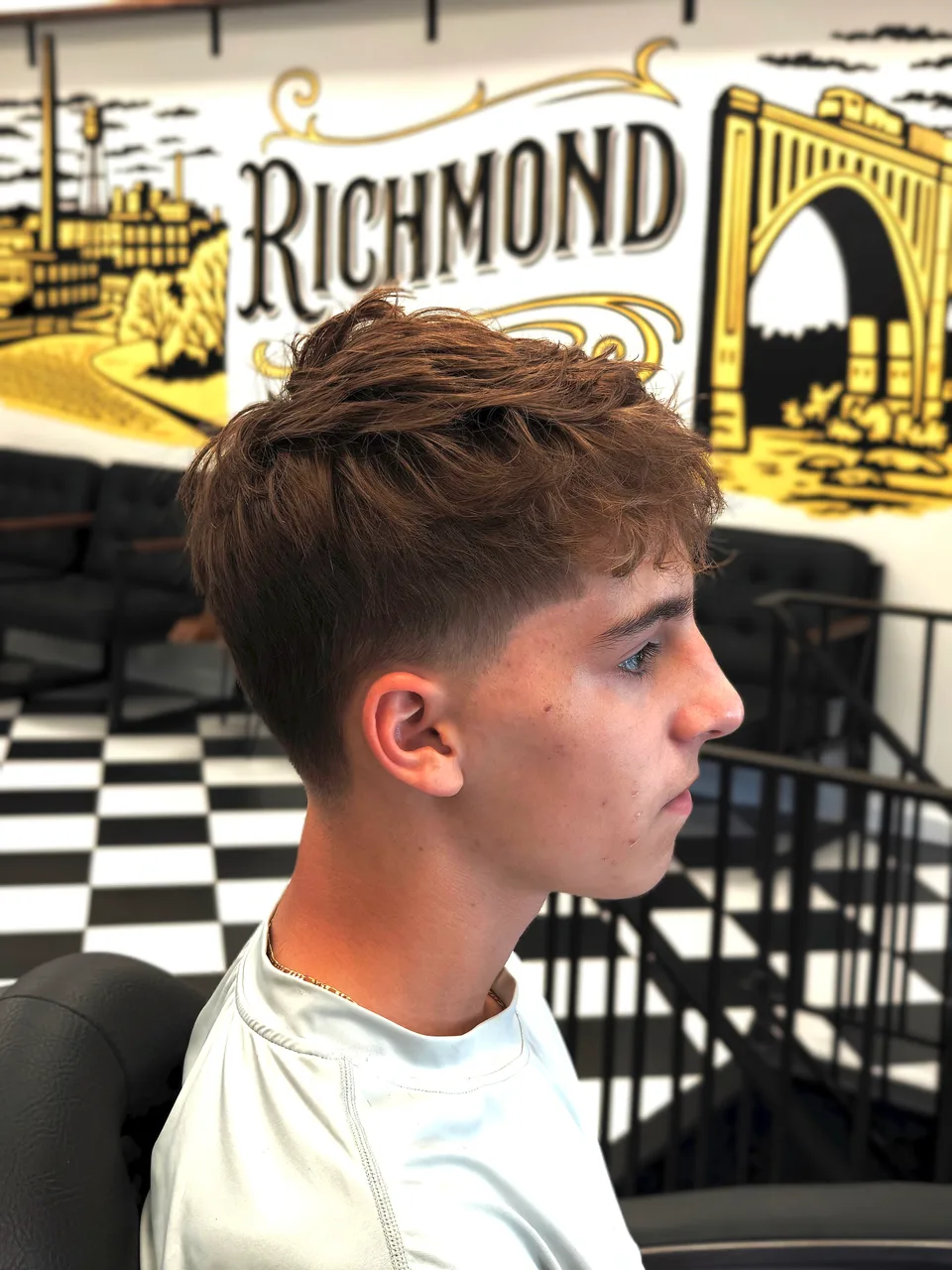 Tousled brown fringe with short tapered sides in front of the Richmond Barbershop mural